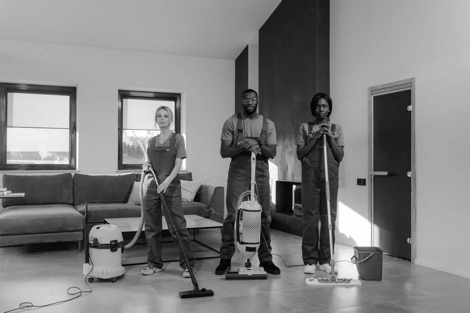 Two women in red overalls vacuuming and sweeping a modern living room.